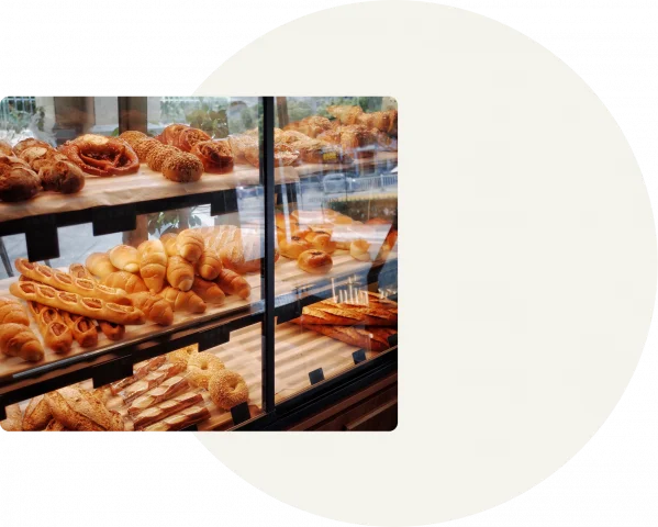 A white circle is displayed on a grey background with a square on the left-hand side displaying croissants in the glass display shelves of a bakery.