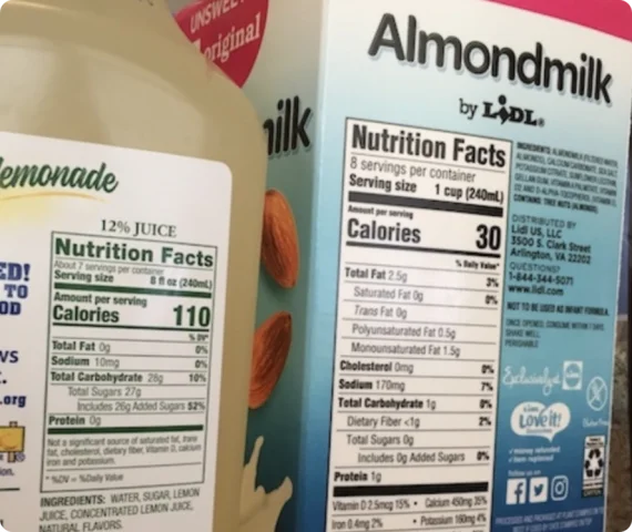 An almond milk bottle and lemonade bottle are standing next to each other, with the nutrition labels clearly depicted on the sides of the bottles.