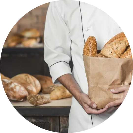 A chef holding a bag of bread in a bakery.