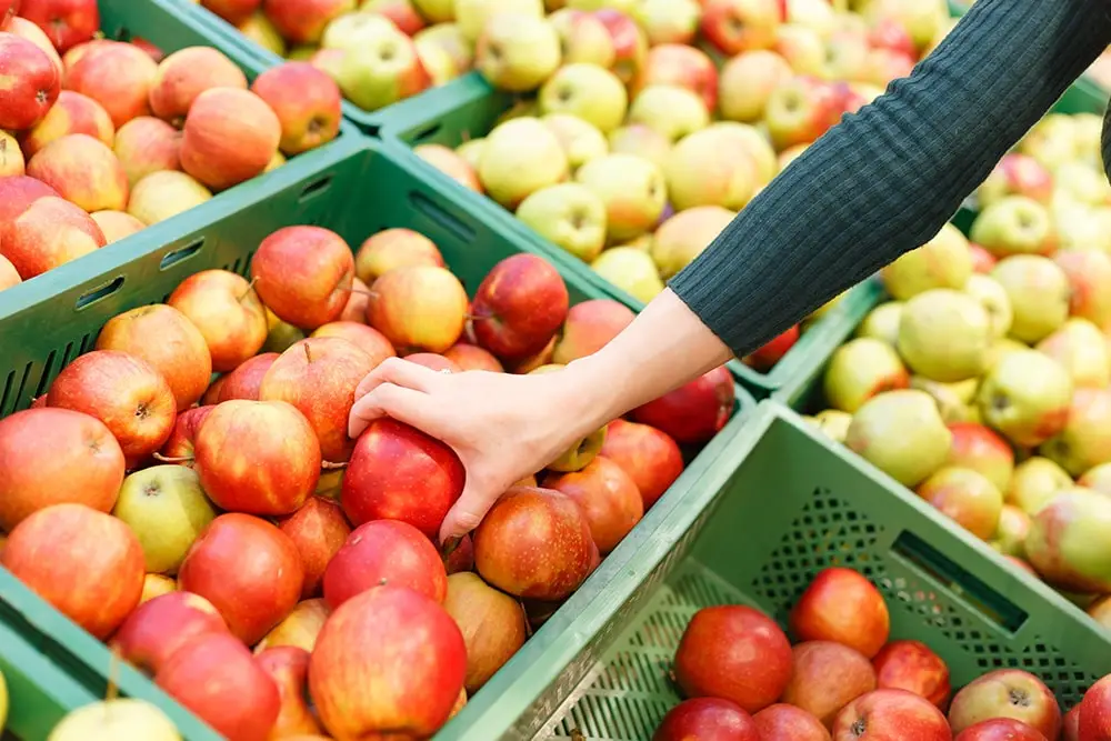 Close-up view of a woman's hand selecting an apple in a supermarket.