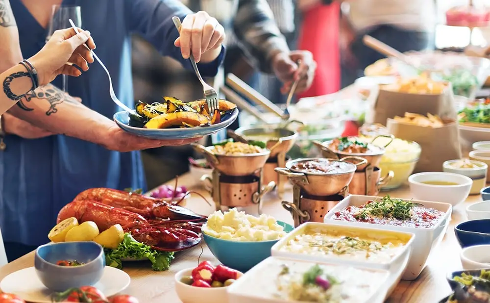 People lined up and placing food from a buffet on their plates.