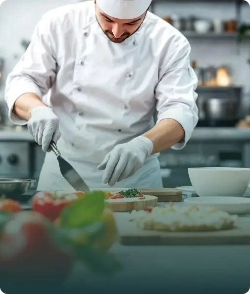 A chef in a white uniform preparing food in a commercial kitchen, illustrating culinary school practicals.