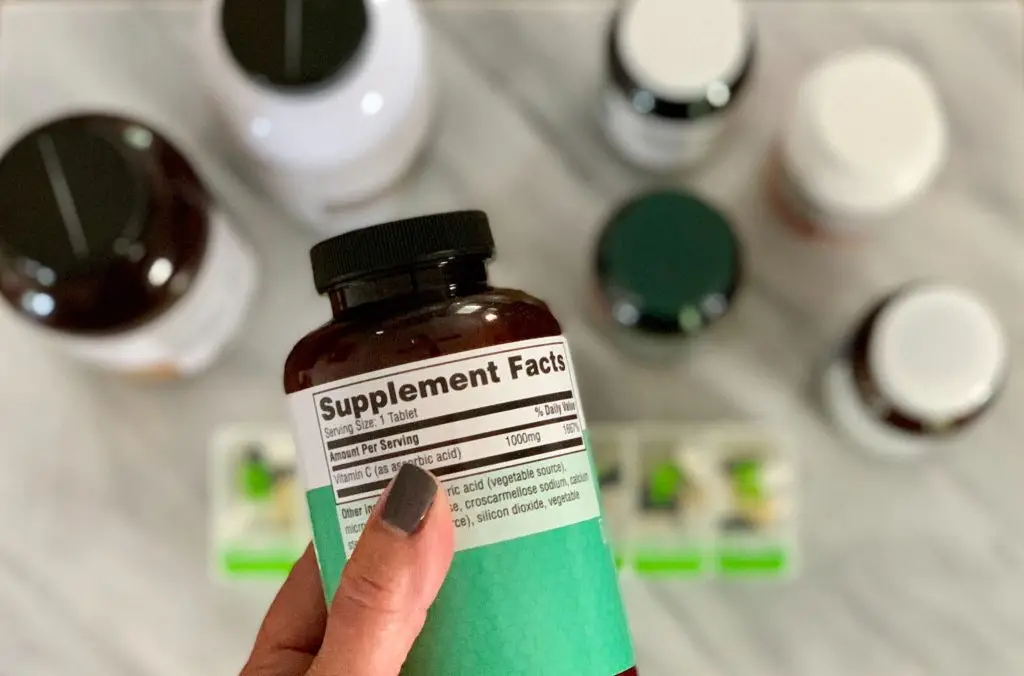 A hand holding a brown and green bottle of supplements, with the ‘Supplement Facts’ label visible.
