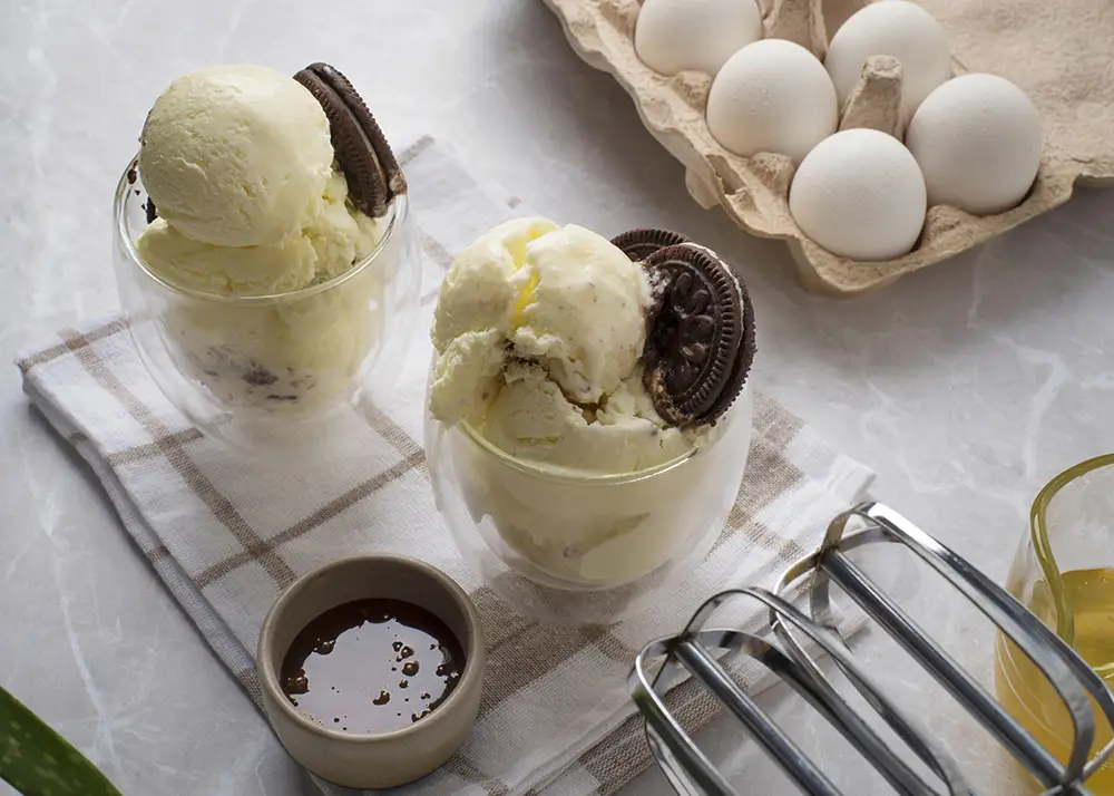 French vanilla ice cream scoops with cookie pieces beside eggs, egg yolks, and vanilla, the custard base ingredients